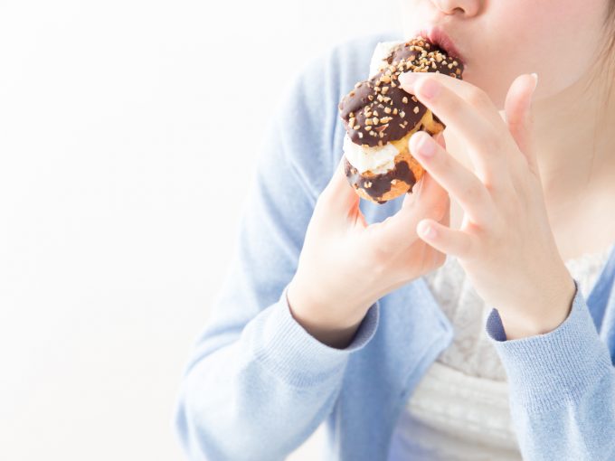 食べ過ぎてしまうドーナツを食べる女性