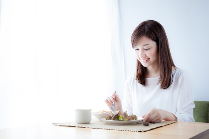 朝日を浴びて朝食を食べる痩せた女性