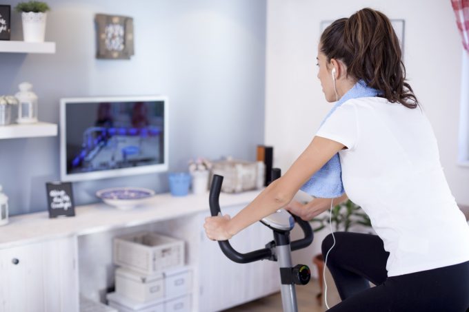 テレビを見ながらエアロバイクを漕ぐ女性