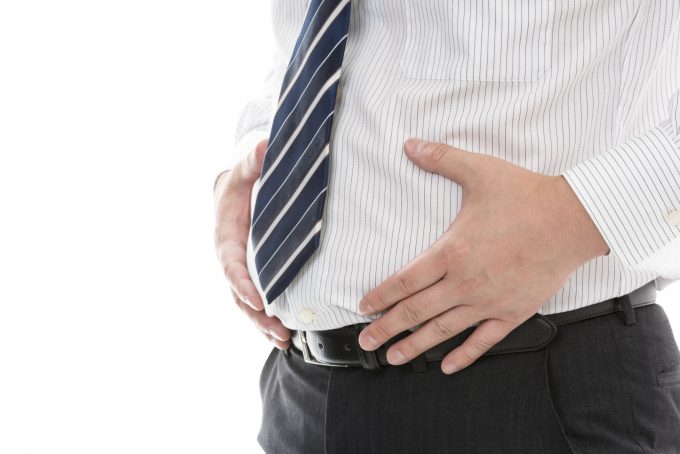 お腹に手をあてる太っているスーツ姿の男性